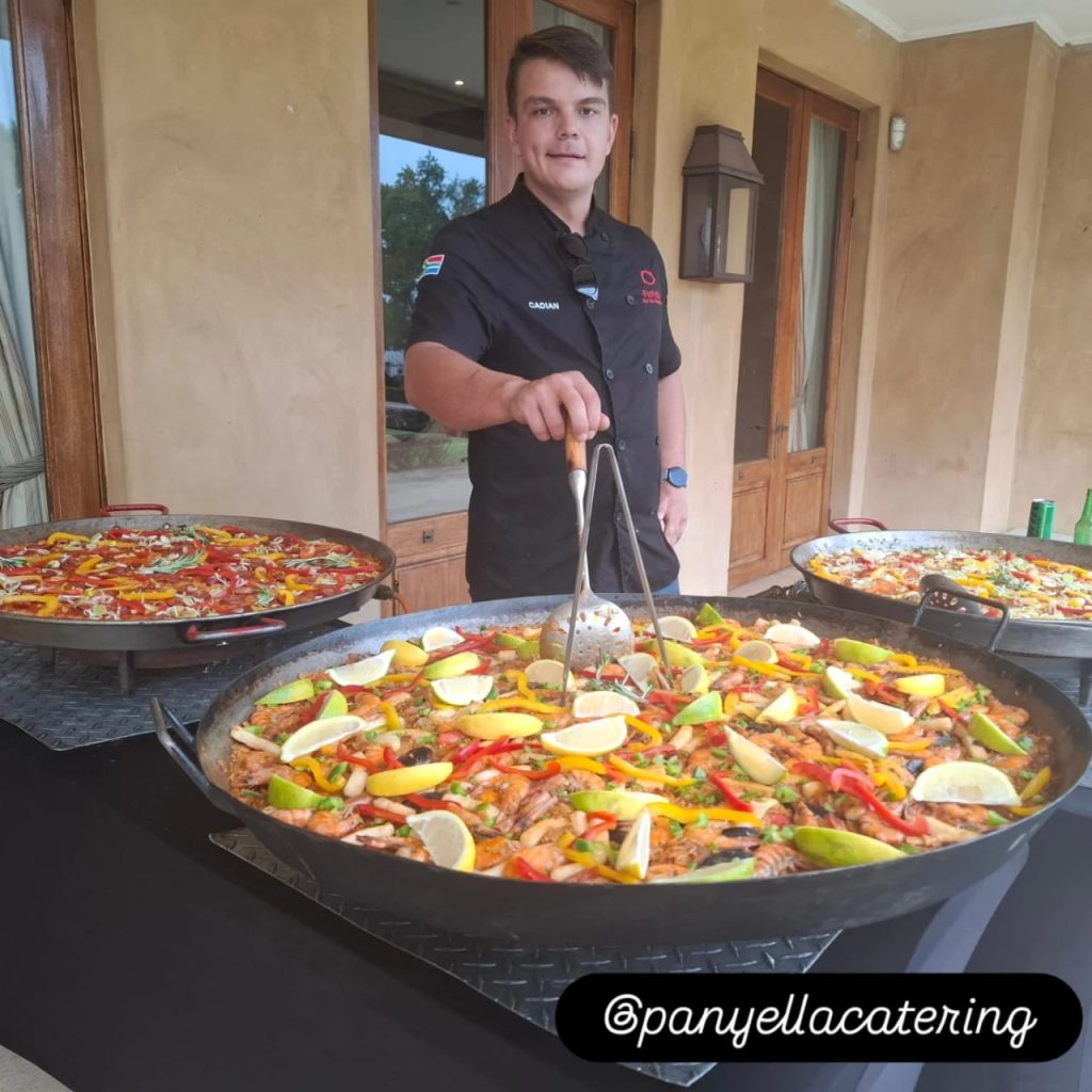 Chef Cadian standing behind large seafood paella pans at a catered event