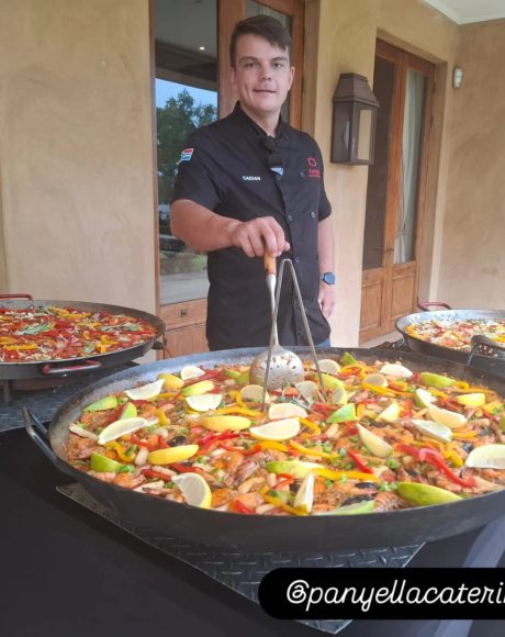 Chef Cadian standing behind large seafood paella pans at a catered event