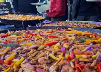 Large seafood paella pans being served fresh at a corporate function, topped with prawns, peppers, and herbs while guests gather around the live cooking station.