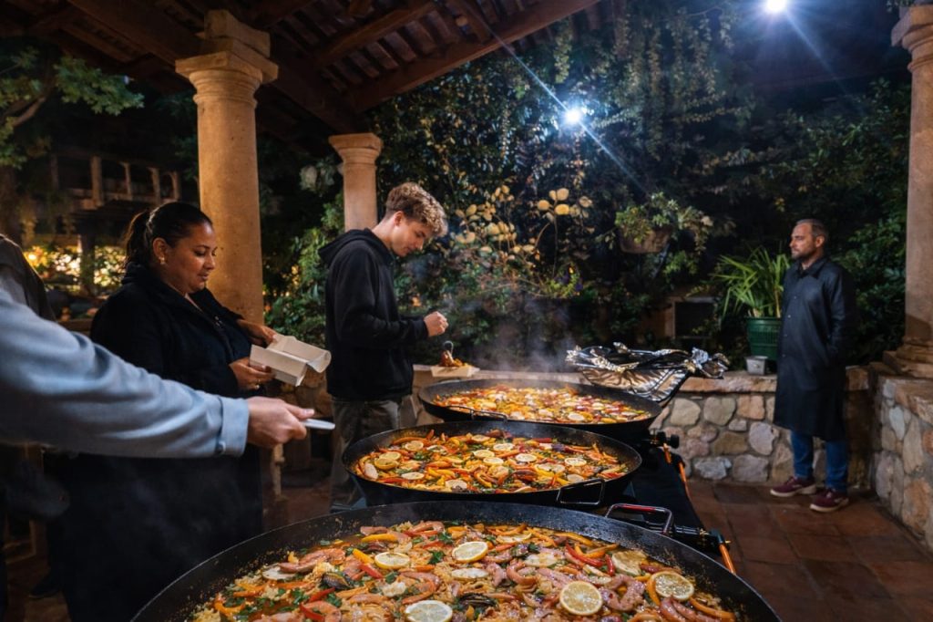 Guests gathered around multiple paella pans during a catered event