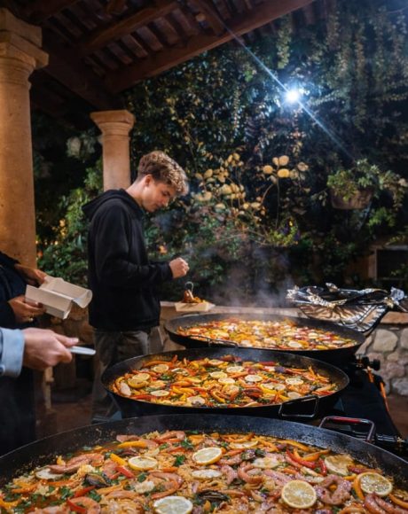 Guests gathered around multiple paella pans during a catered event