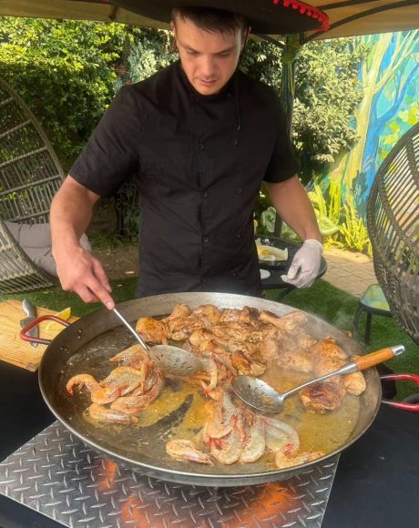 Chef preparing chicken and seafood paella in a large pan at an event